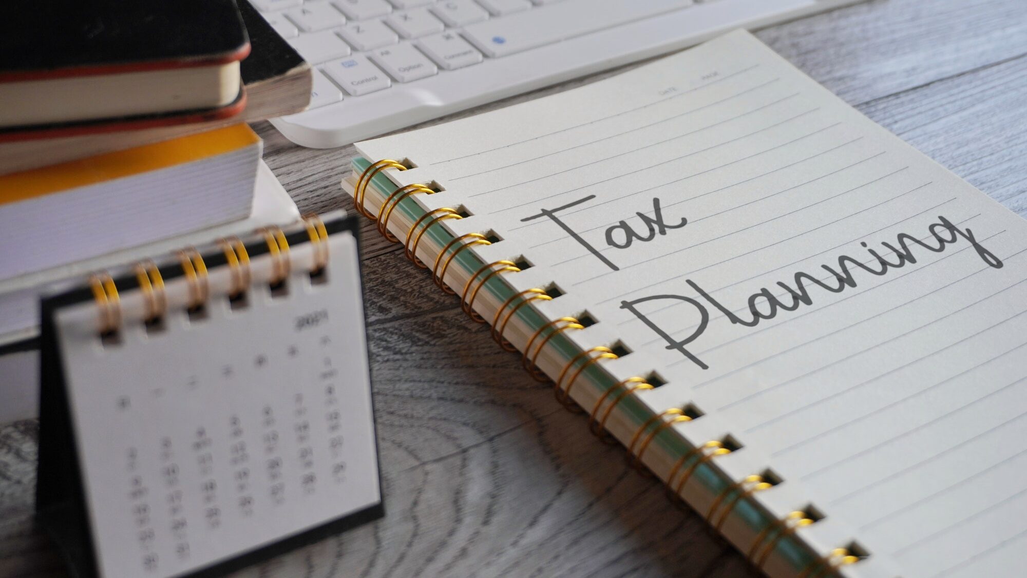 Closeup image of notebook with text TAX PLANNING and calendar on office desk.